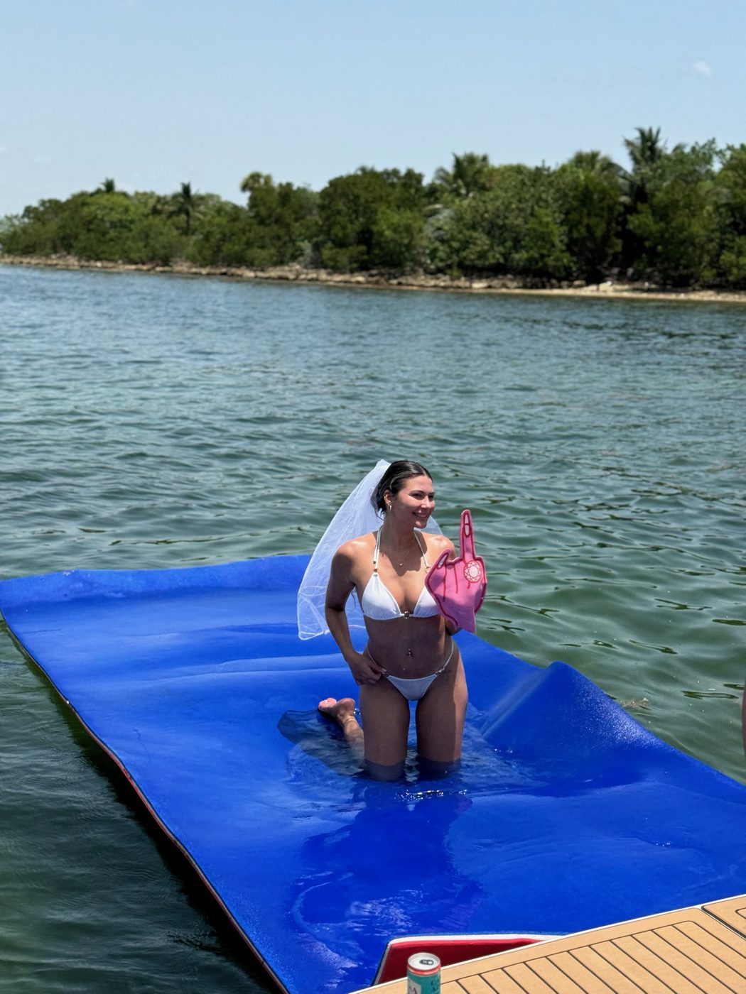 Bride wearing a veil standing on a floating mat in the water at a Miami sandbar