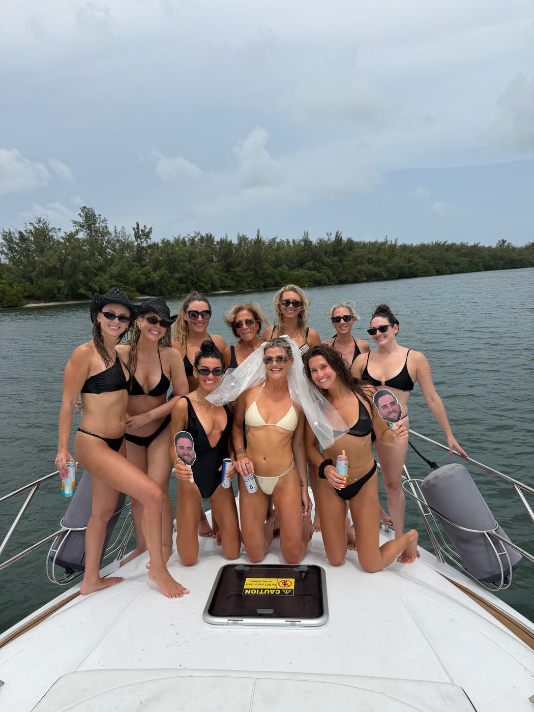 Bachelorette party group posing with veil and photo props on the bow of a yacht in Miami