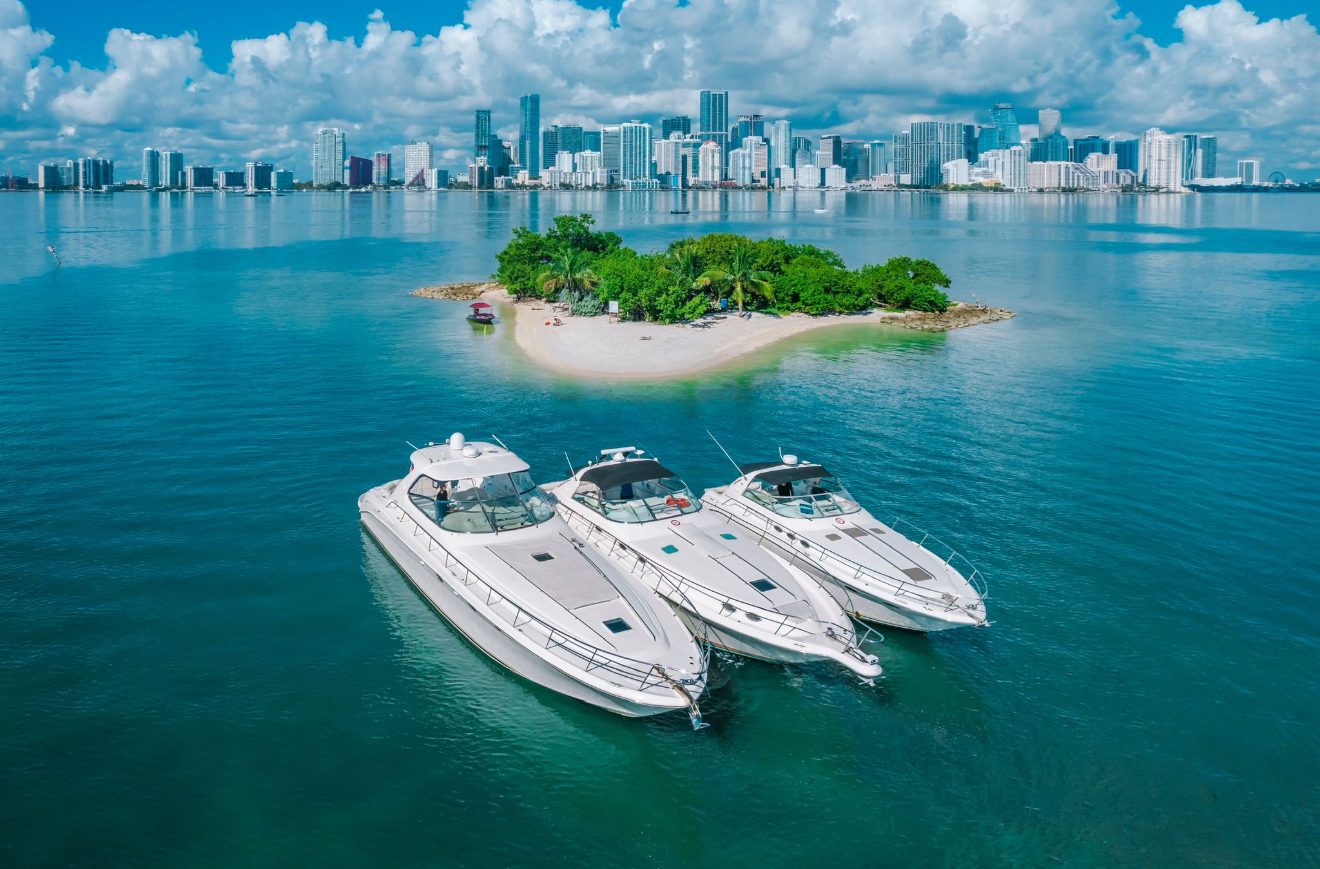 Three yachts tied up together at a Miami sandbar with the Downtown skyline behind